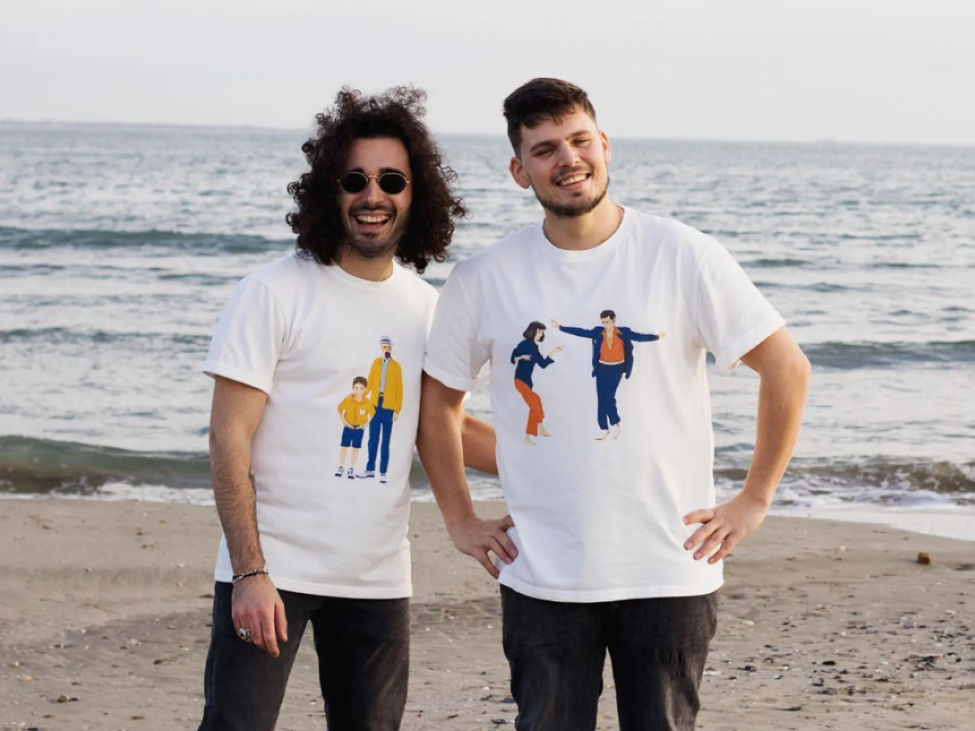 Two friends laughing on the beach, wearing the Father & Son and The Lovers WAAS tees