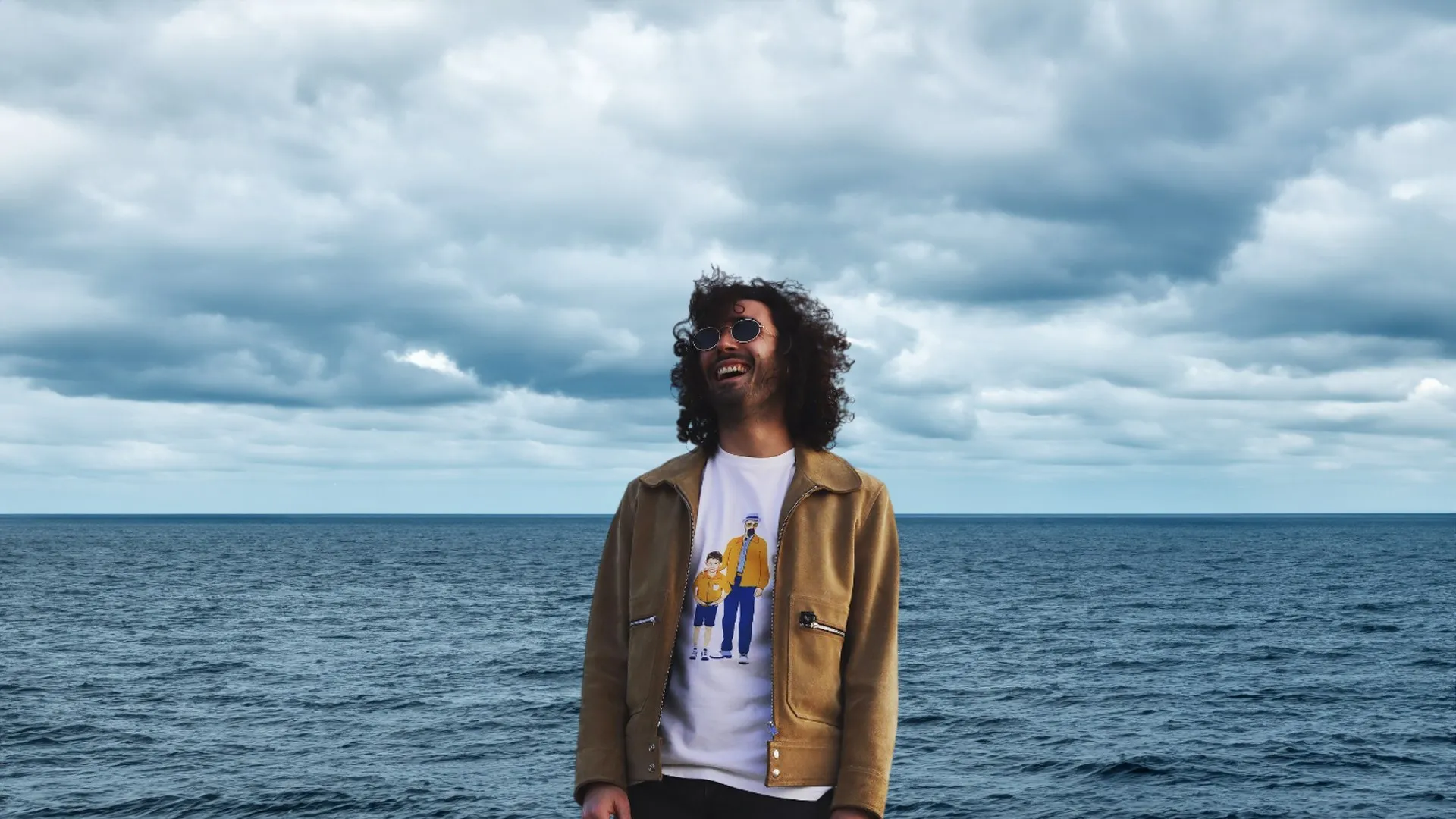 Laughing by the sea, wearing the Father & Son tee under a suede jacket