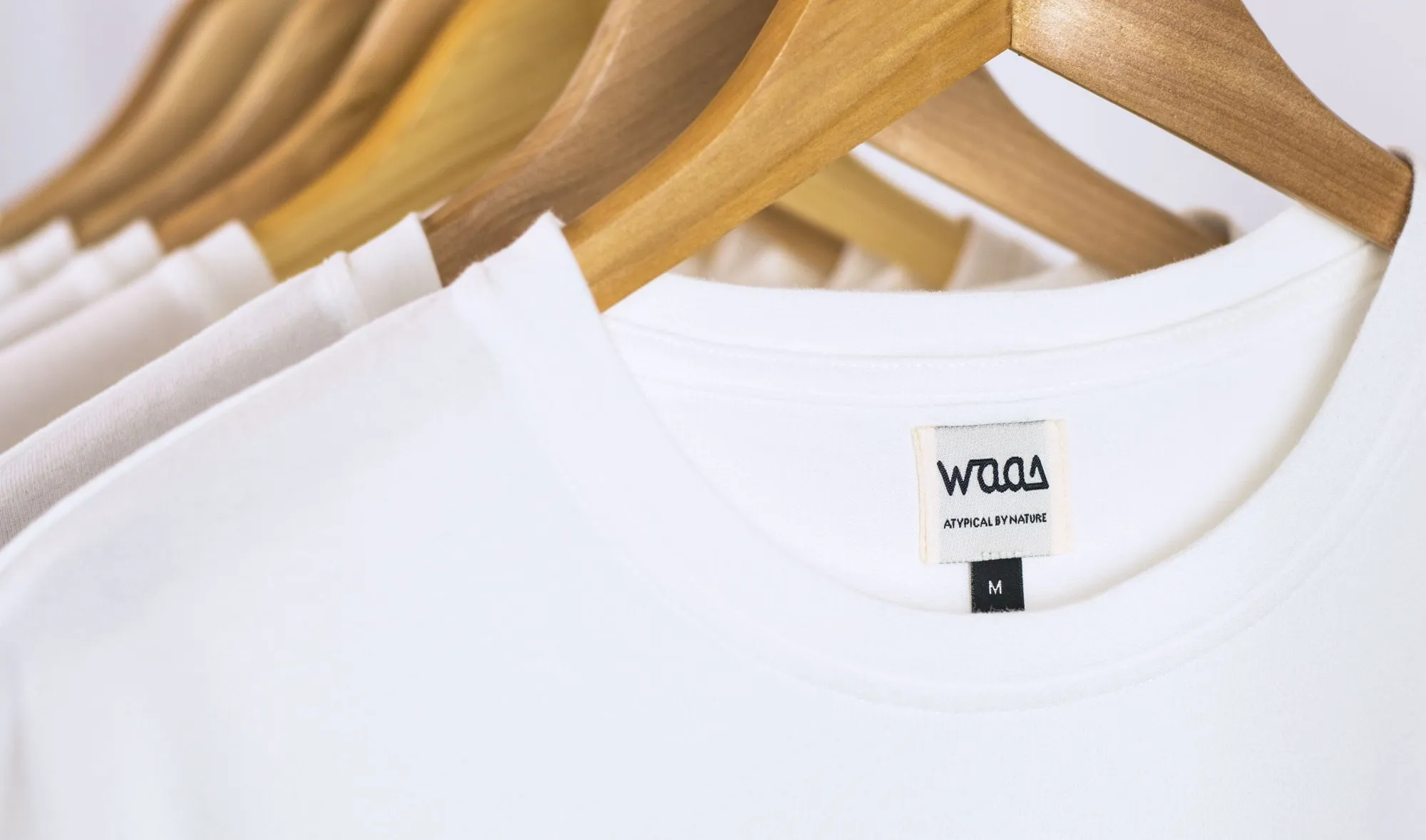 WAAS tees on wooden hangers, close-up on the woven neck label